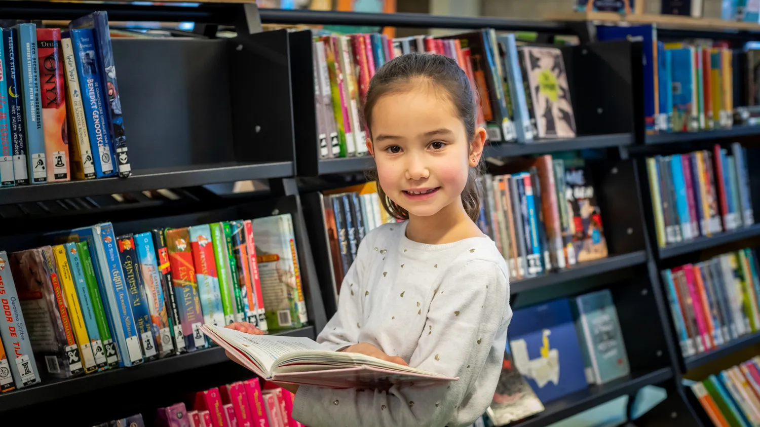 Meisje met open boek bij boekenkast