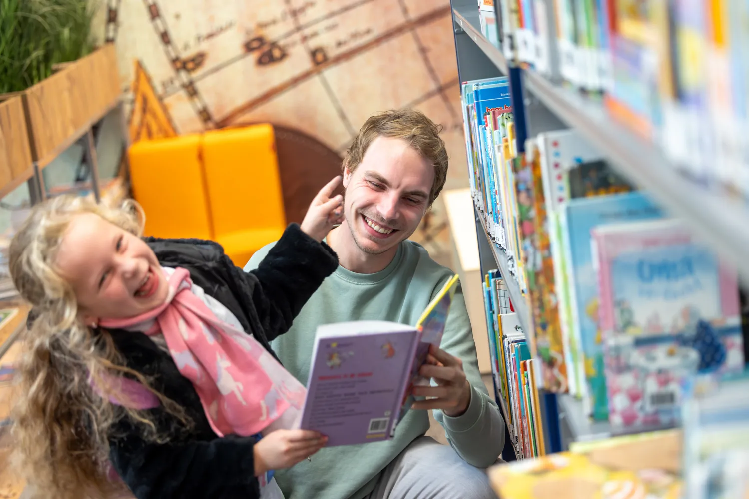 Lachende leerkracht en kind bij boekenkast