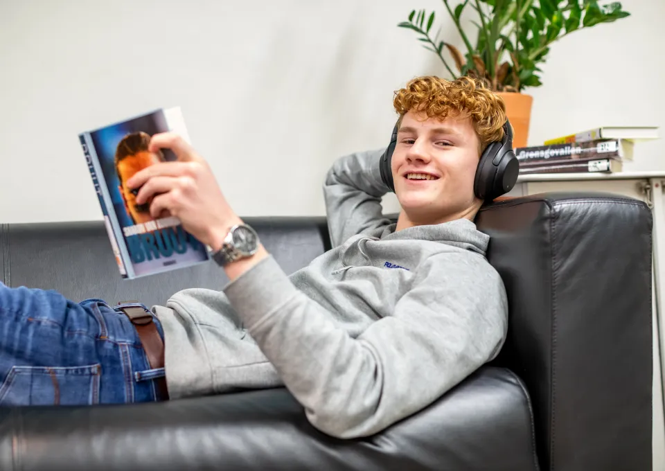 jonge man liggend op bank met koptelefoon en boek