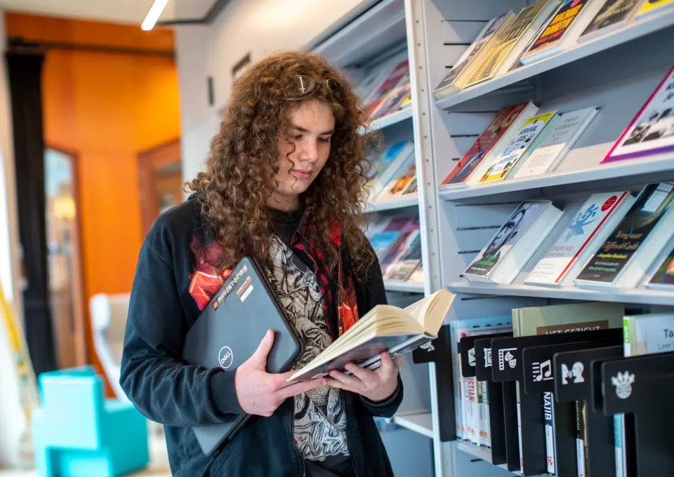 jongen met laptop bij boekenkast