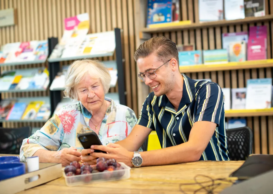 Jonge man met mobiel geeft uit aan oudere dame 