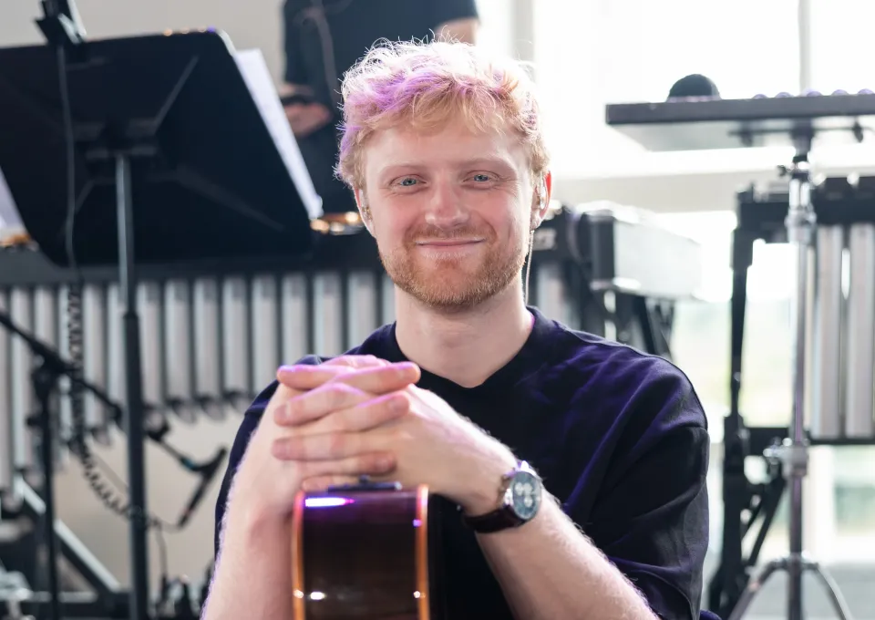 foto van jongeman met rossig haar en kort baardje. Zittend met een gitaar op schoot